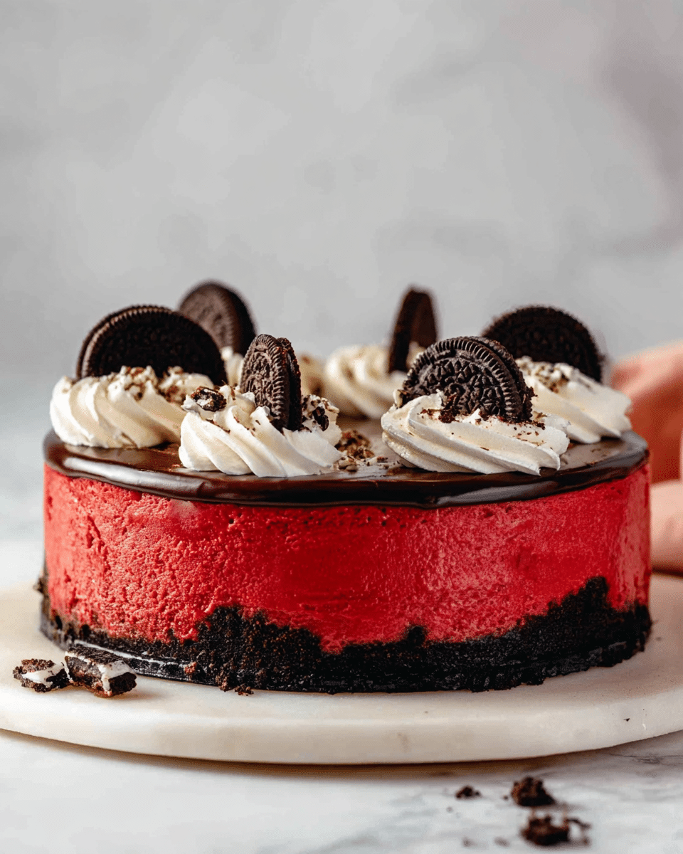 This dessert is a round cheesecake with three clear layers visible from the cut side. The bottom layer is a dark chocolate crumb crust, thick and firm. The middle layer is a smooth, vibrant red cheesecake filling, dense and creamy in texture. The top layer is a glossy dark chocolate ganache, spread evenly over the cheesecake. On top, there are swirls of white whipped cream around the edge, each swirl topped with a whole black and white sandwich cookie. Crushed cookie pieces are sprinkled in the space between the whipped cream swirls. The cake sits on a white marbled surface. photo taken with an iphone --ar 4:5 --v 7