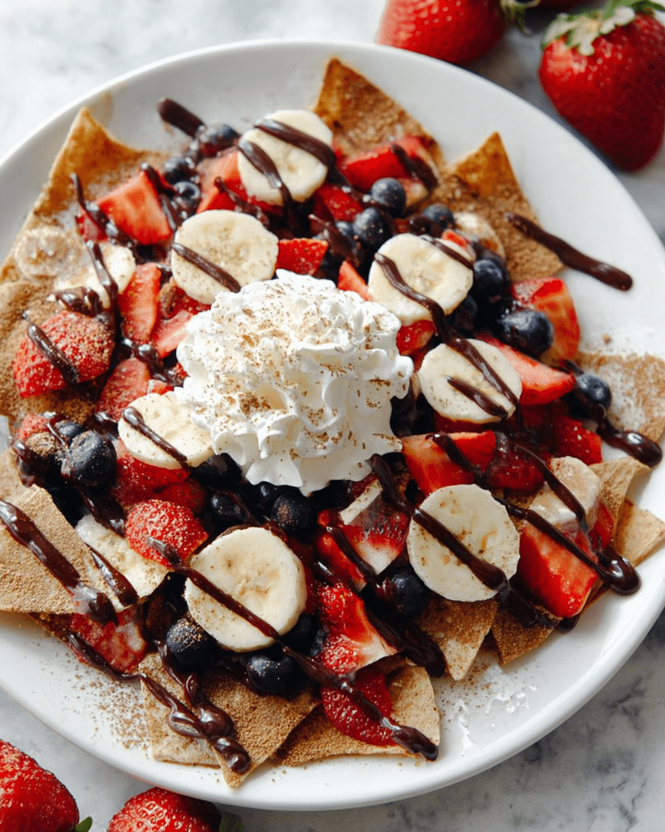 The dish features a white plate filled with a base layer of cinnamon-spiced triangular chips in a warm brown color, topped with bright red sliced strawberries and pale yellow banana slices scattered evenly. Small, round dark blue blueberries add color contrast across the plate. A thick drizzle of dark chocolate sauce runs over the entire dish in uneven lines. At the center, there is a dollop of creamy white whipped cream sprinkled lightly with cinnamon. The plate is set on a white marbled surface with whole strawberries in the background for a fresh touch. photo taken with an iphone --ar 4:5 --v 7
