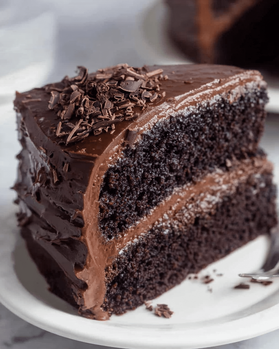 A close-up view of a two-layer chocolate cake slice on a white plate, placed on a white marbled surface. The bottom and top layers are dark, moist chocolate sponge cake. Between the layers is a smooth, thick layer of milk chocolate frosting with a creamy texture. The outside of the slice is covered in a rich, glossy dark chocolate frosting that has visible swirls and waves. On top, there are small dark chocolate shavings scattered, adding texture and decoration. Photo taken with an iphone --ar 4:5 --v 7