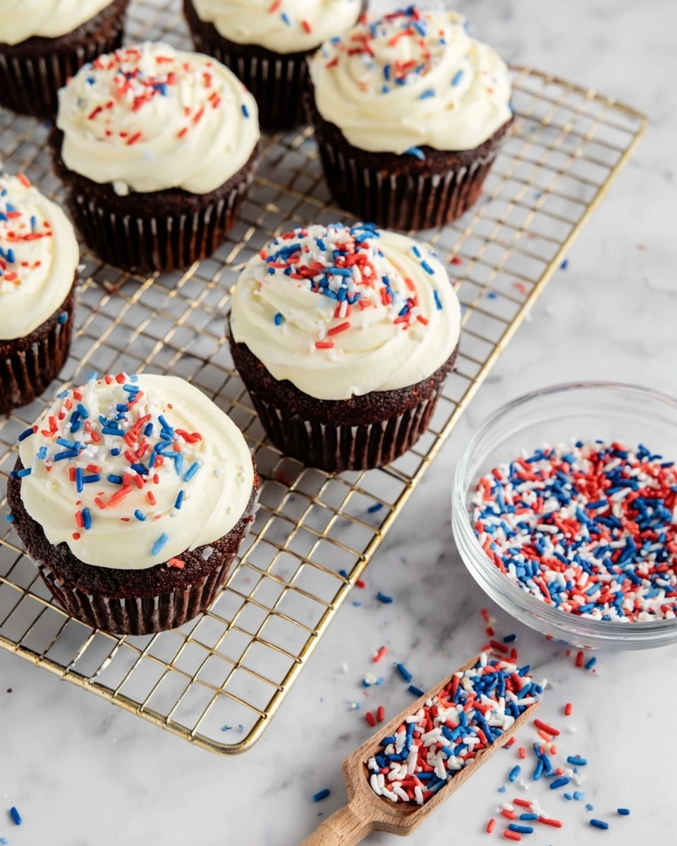 The image shows six chocolate cupcakes placed on a gold wire cooling rack over a white marbled texture. Each cupcake has a base layer of dark brown chocolate cake, topped with a generous swirl of smooth white frosting. The frosting is sprinkled with red, white, and blue cylindrical sprinkles scattered evenly across the tops. To the side, there is a clear bowl filled with the same red, white, and blue sprinkles and a small wooden scoop resting inside. Some sprinkles are also scattered around on the cooling rack and marbled surface. photo taken with an iphone --ar 4:5 --v 7