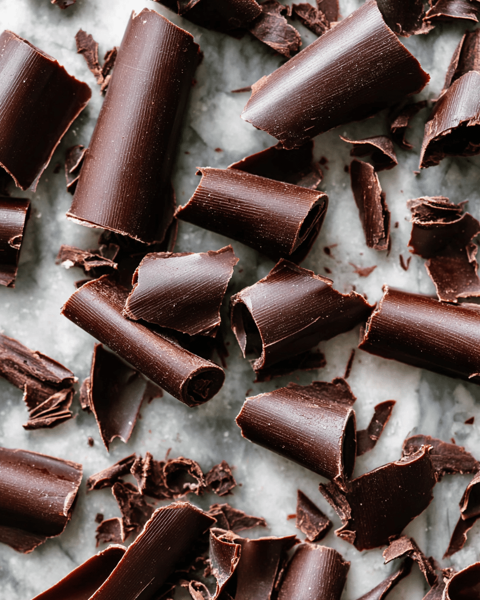 The image shows many pieces of dark chocolate curls spread out on a white marbled surface. Each chocolate curl has a smooth, shiny texture with some edges torn or slightly rough. The curls vary in size and shape, some look like rolled strips while others are folded or flat flakes. The rich dark brown color of the chocolate contrasts with the light marbled background, making the curls stand out clearly. photo taken with an iphone --ar 4:5 --v 7