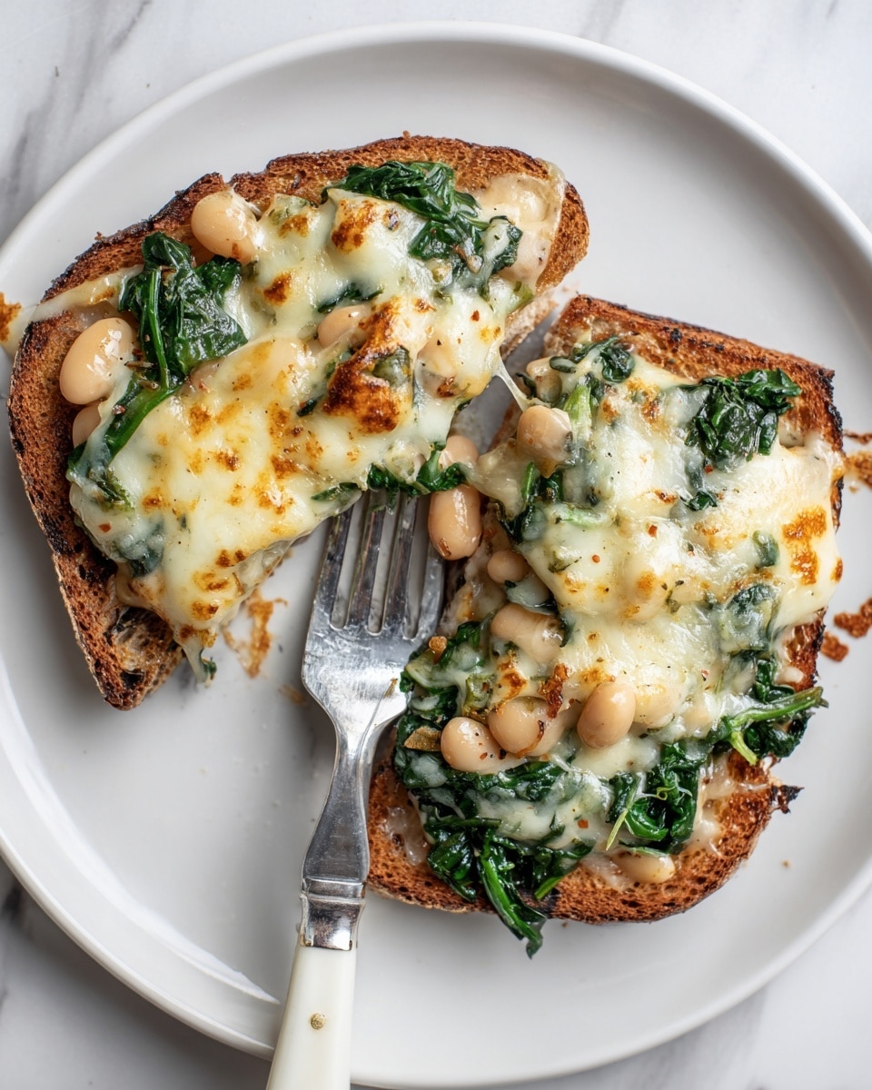 The image shows two rectangular pieces of toasted brown bread, each topped with a thick layer of melted cheese that is golden and bubbly. Under the cheese, there is a green leafy layer visible, likely spinach or kale, along with some white beans and possibly tomato bits mixed in. One piece has a bite taken out of it, with a portion held on a silver fork featuring a white handle placed on the white plate. The surface underneath the plate is a white marbled texture. Photo taken with an iphone --ar 4:5 --v 7