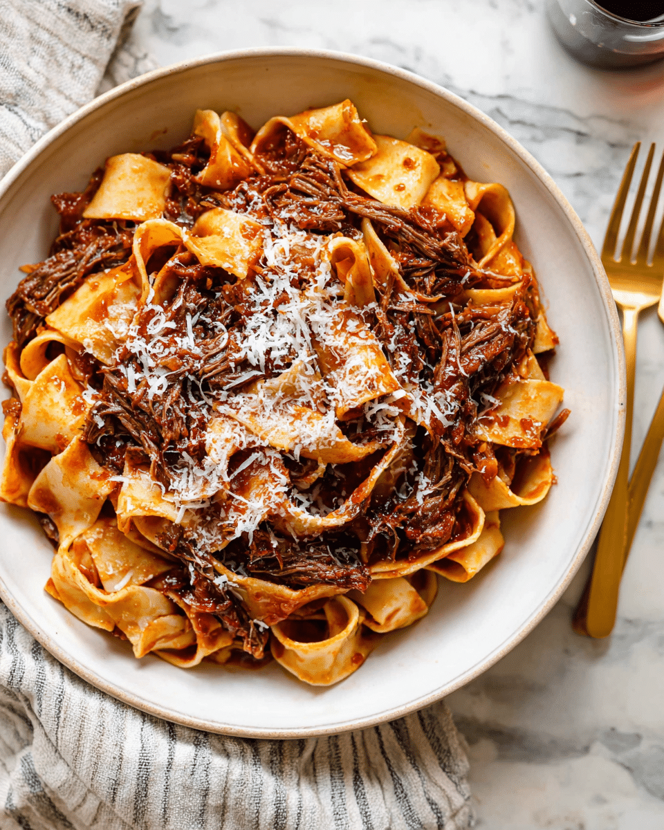 In the white bowl, there is one layer of wide, flat pasta ribbons that are soft tan with light browning edges, tangled and twisted together. On top and mixed into the pasta are thick strands of dark brown shredded meat, covered in a rich, reddish-brown sauce that pools slightly beneath the pasta. The dish is finished with a thin sprinkle of finely grated white cheese scattered evenly over the top. The bowl sits on a white marbled surface, with a striped cloth and a golden fork nearby. Photo taken with an iphone --ar 4:5 --v 7