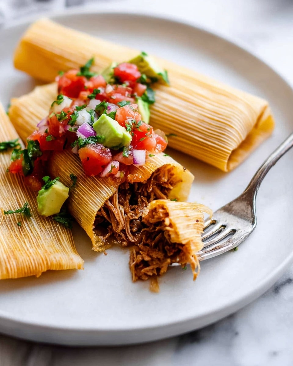 The image shows two light golden brown tamales on a white plate placed on a white marbled surface. One tamale is whole with a soft texture, and the other is cut open, showing a dark brown shredded meat filling inside. On top of the tamales is a colorful salsa made of bright red diced tomatoes, green avocado pieces, red onion chunks, and chopped green herbs, adding a fresh look. A shiny silver fork is resting partly on the plate near the tamales, holding a small piece of tamale. The scene is bright and clear, with light highlighting the textures of the food. Photo taken with an iphone --ar 4:5 --v 7