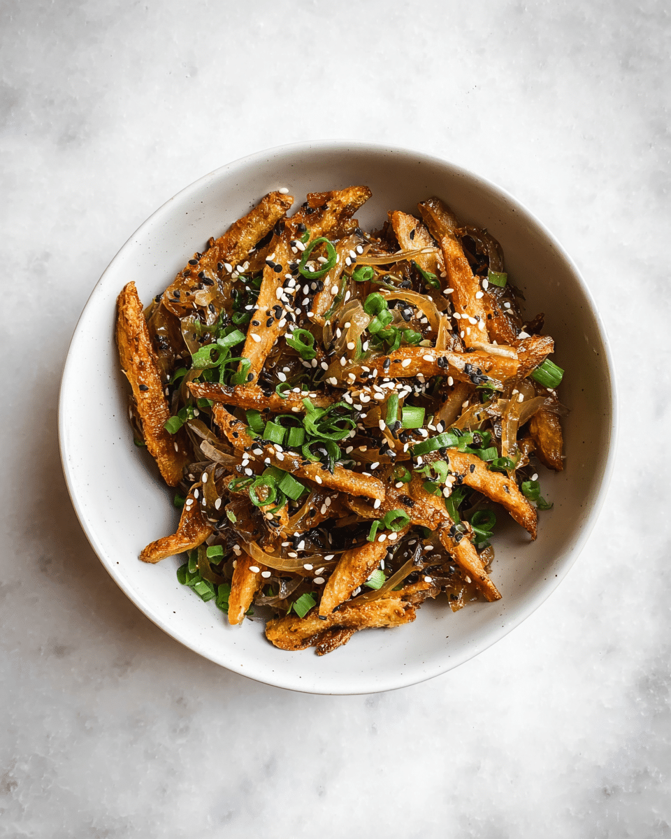 A white bowl filled with two main layers: the bottom layer is golden-brown fried strips that appear crispy and slightly charred at edges, while the top layer is scattered with thin, translucent sautéed onions, sprinkled evenly with white and black sesame seeds, and small bright green chopped scallions, all sitting on a white marbled surface. photo taken with an iphone --ar 4:5 --v 7