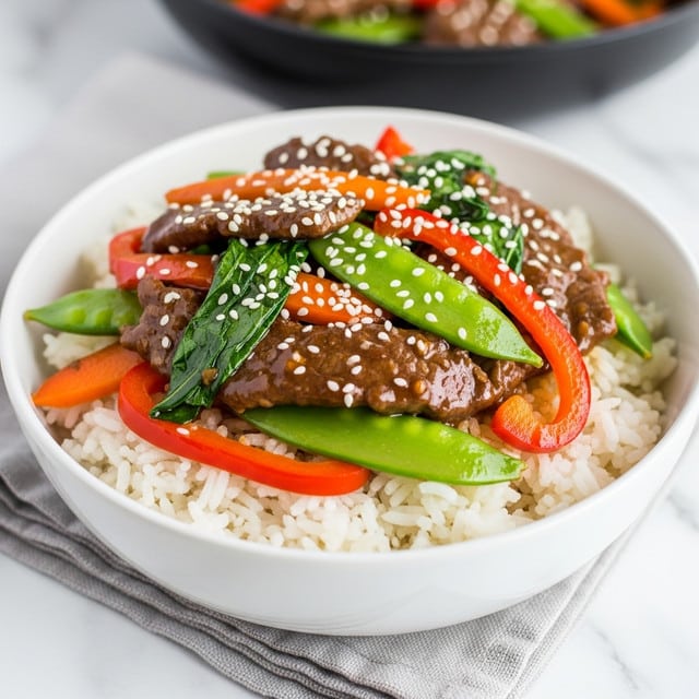 A white bowl filled with a base layer of white steamed rice showing soft and fluffy texture, topped with a colorful stir-fry mix. The stir-fry includes slices of tender brown beef coated in a shiny sauce, bright red and orange bell pepper strips, green leafy vegetables, and chunks of green snap peas. The dish is sprinkled with white sesame seeds, adding a slight crunch on top. The bowl rests on a light gray cloth napkin placed on a white marbled surface. In the background, a blurred black pan holds more stir-fried vegetables. Photo taken with an iphone --ar 4:5 --v 7