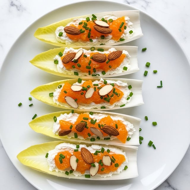A white plate with five layers of endive leaves arranged in a line, each leaf holding a filling. The bottom layer is the pale yellow endive leaf with a slightly curved and smooth texture. On top of each leaf is a creamy white layer of cheese or spread, soft and smooth. Scattered on the cheese are small bright orange chunks of mandarin or similar fruit, adding a juicy and glossy texture. Thin, light brown almond slices are placed on top, giving a crunchy texture. Small green chives are sprinkled over all the layers, adding a fresh and slightly rough texture. The background has a white marbled texture. photo taken with an iphone --ar 4:5 --v 7