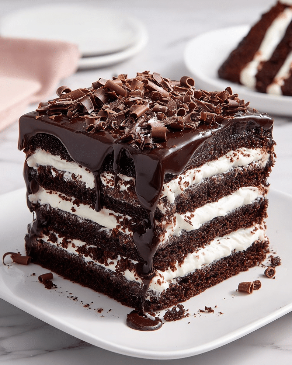 A tall, square chocolate cake with four distinct dark brown layers looks rich and moist, each separated by thick, creamy white filling. The top layer is covered with a smooth, glossy dark chocolate ganache that drips slightly over the edges. Small curls and shavings of milk chocolate are scattered generously on top, adding texture and decoration. The cake sits on a white square plate placed on a white marbled surface. In the background, there’s a blurred view of a white plate holding a slice of the same cake. Photo taken with an iphone --ar 4:5 --v 7