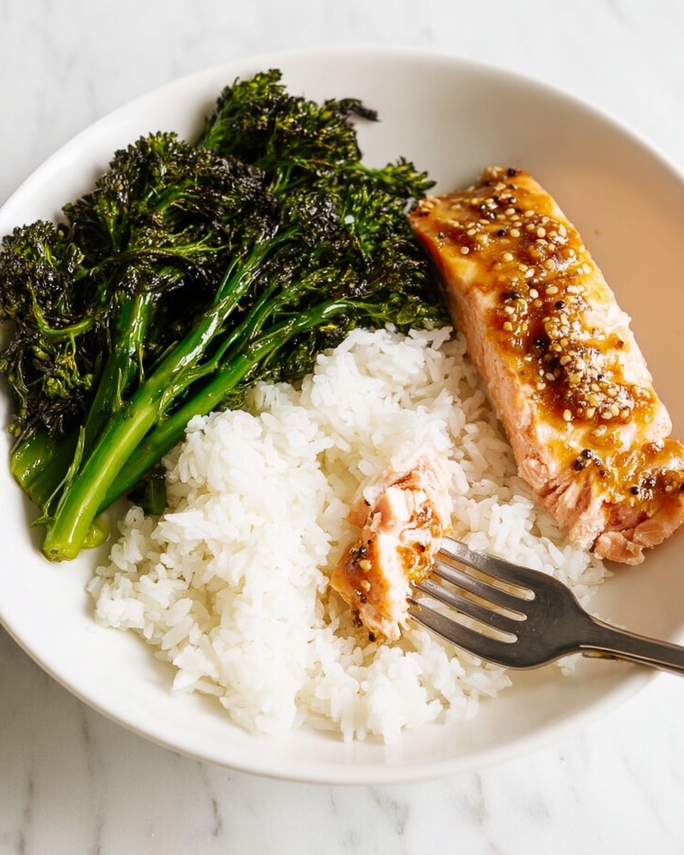 The dish shows a white bowl with three layers: on the bottom left is a soft pile of white rice with fluffy texture, on the top left sits a serving of roasted broccolini with dark green, slightly charred tips and visible garlic pieces, and the right side features a cooked salmon fillet covered with a shiny, grainy mustard glaze, showing light pink flaky fish underneath. A fork is placed on the right side, piercing a piece of the salmon. The whole scene is set on a white marbled surface. photo taken with an iphone --ar 4:5 --v 7