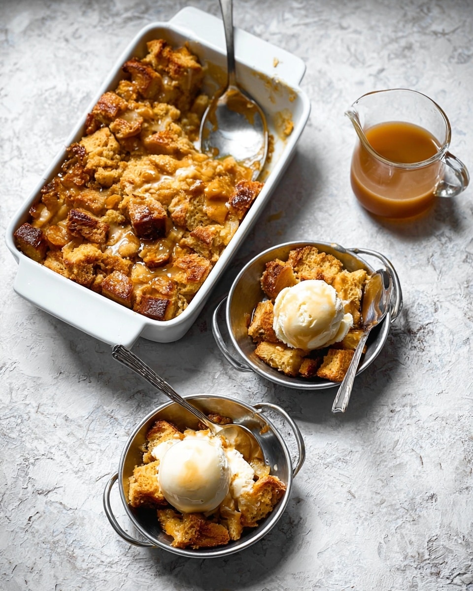 The image shows a golden brown bread pudding with visible chunks of bread soaked and baked, placed in a white ceramic baking dish at the top. Two small silver pans hold servings of the bread pudding; one pan has a scoop of melting white vanilla ice cream on top, while the other has the pudding alone. A silver spoon rests inside each pan. Nearby, there is a small clear glass pitcher containing a light brown sauce, likely caramel or syrup. Everything is set on a white marbled textured surface that contrasts with the warm tones of the dessert. The overall look is cozy and inviting. photo taken with an iphone --ar 4:5 --v 7