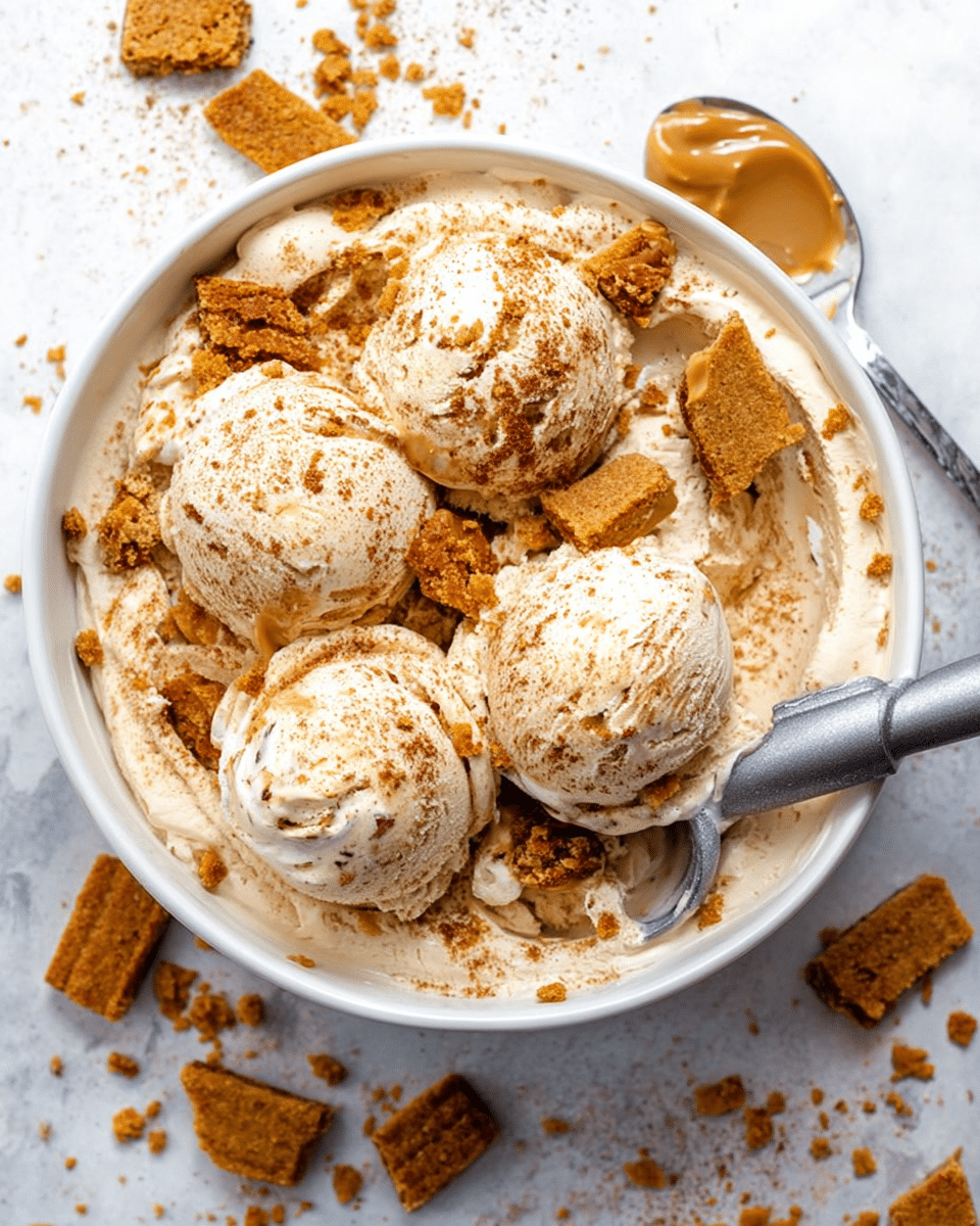 A white bowl filled with creamy beige ice cream that has specks of darker brown swirled throughout, giving it a marbled look; on the top surface, there are scattered crumbled golden brown cookie pieces and a light dusting of cinnamon powder. Five scoops of ice cream are partially rounded and resting on the surface, with a metal ice cream scoop placed inside the bowl on the right side. Around the bowl on a white marbled background, there are broken pieces of the same golden brown cookies and a white spoon with a dollop of creamy peanut butter on it. Photo taken with an iphone --ar 4:5 --v 7