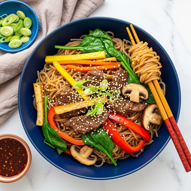 A dark blue bowl filled with glossy, light brown glass noodles mixed with pieces of dark brown beef, yellow tofu strips, orange carrot slices, red bell pepper strips, green spinach leaves, and sliced beige mushrooms, all topped with white sesame seeds and thinly sliced green onions. On the right edge of the bowl, a pair of red-brown chopsticks holds a small bundle of noodles. The bowl sits on a white marbled surface with a light brown cloth napkin near the top left, a small blue bowl with sliced green onions at the top right, and a small round light brown bowl with dark red sauce on the bottom left. Photo taken with an iphone --ar 4:5 --v 7