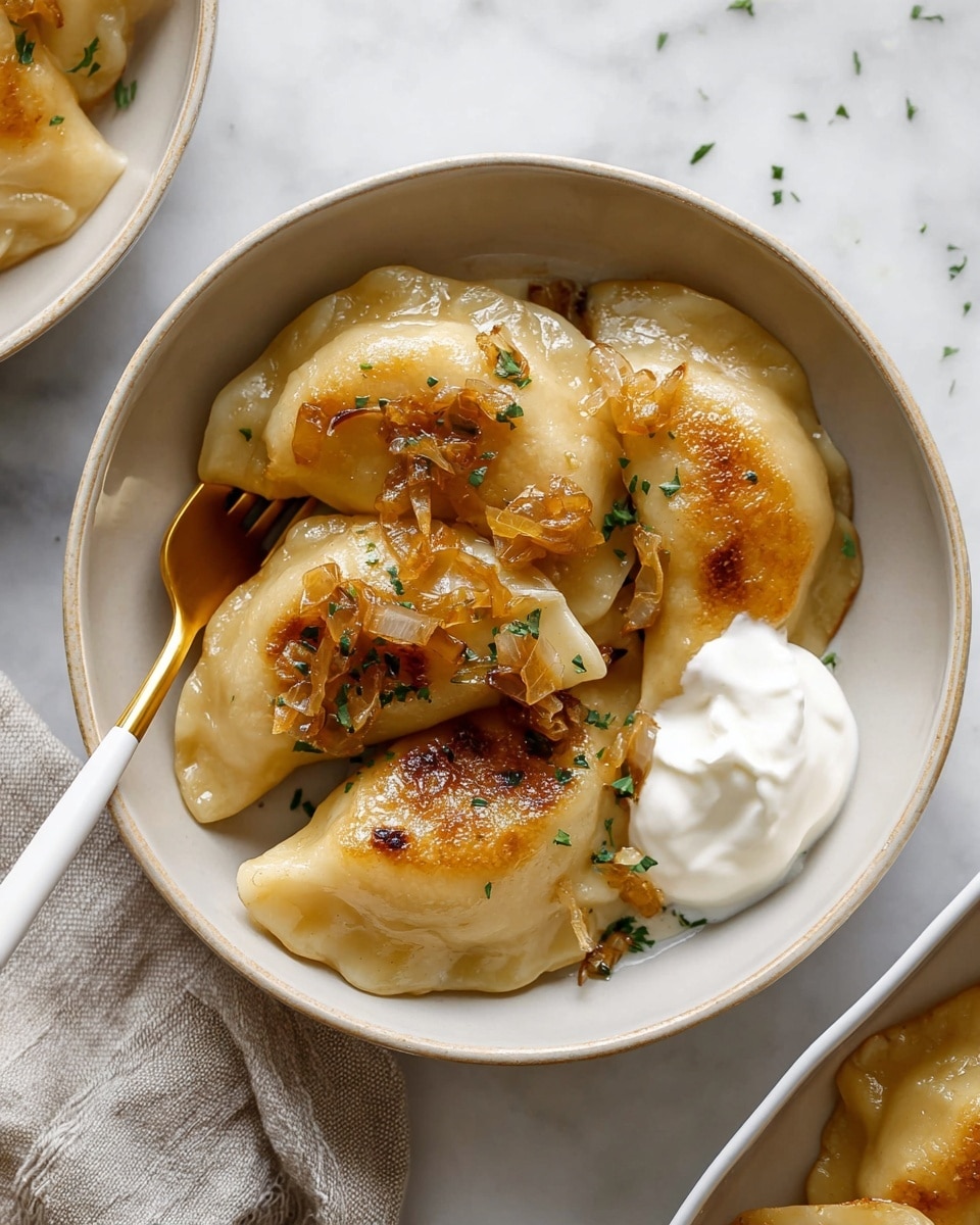A white bowl filled with four golden-brown pierogies, each with a slightly crispy texture and browned edges from frying. The pierogies are topped with small pieces of caramelized onion and sprinkled with green herbs. A dollop of smooth white sour cream sits beside the pierogies on the right side of the bowl. A gold spoon with a white handle rests inside the bowl on the left side, slightly touching the pierogies. The bowl is placed on a white marbled surface with part of a white dish to the right showing more pierogies. Photo taken with an iphone --ar 4:5 --v 7