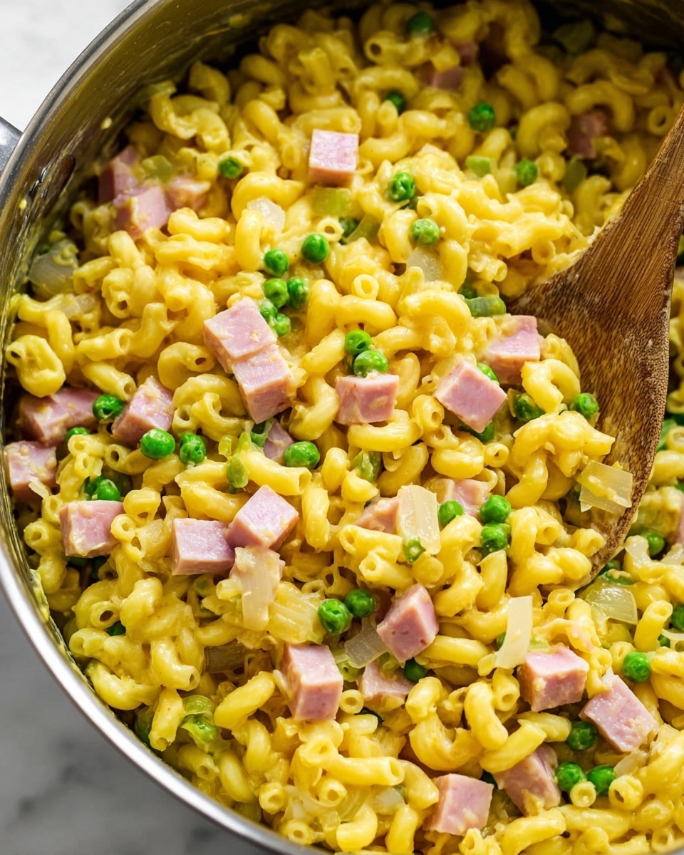 The image shows a close-up of a cooked macaroni dish in a pot. The dish has three layers mixed together: the base is bright yellow macaroni pasta, soft and curved, making up the majority of the dish. Scattered throughout are small, green peas adding pops of color and smooth texture. Light pink cubes of ham are evenly spread on top, giving the dish a chunky appearance. There are also translucent small pieces of cooked onion mixed evenly among the macaroni and peas. A wooden spoon is partially visible on the right side, stirring the ingredients. The background is a white marbled texture photo taken with an iphone --ar 4:5 --v 7