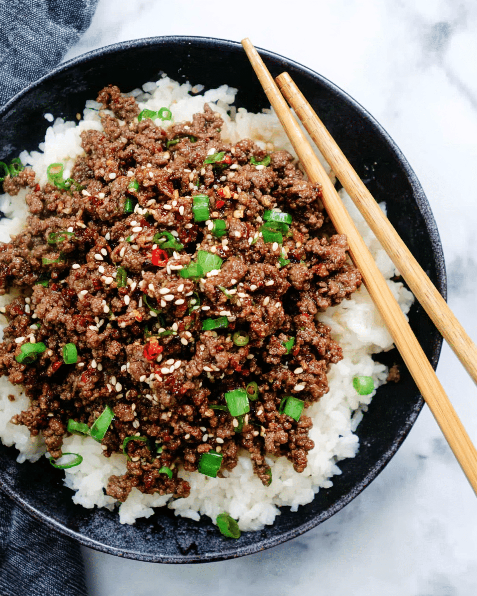 A close-up top view of a black bowl filled with two main layers: the bottom layer is a bed of fluffy white rice with a soft, slightly sticky texture, and the top layer is a generous portion of cooked ground beef that is brown with slight caramelized edges, sprinkled with small green onion pieces and sesame seeds, with a touch of red chili flakes for color. Two light brown wooden chopsticks rest on the right side, partly inserted into the beef, all set on a white marbled surface. photo taken with an iphone --ar 4:5 --v 7