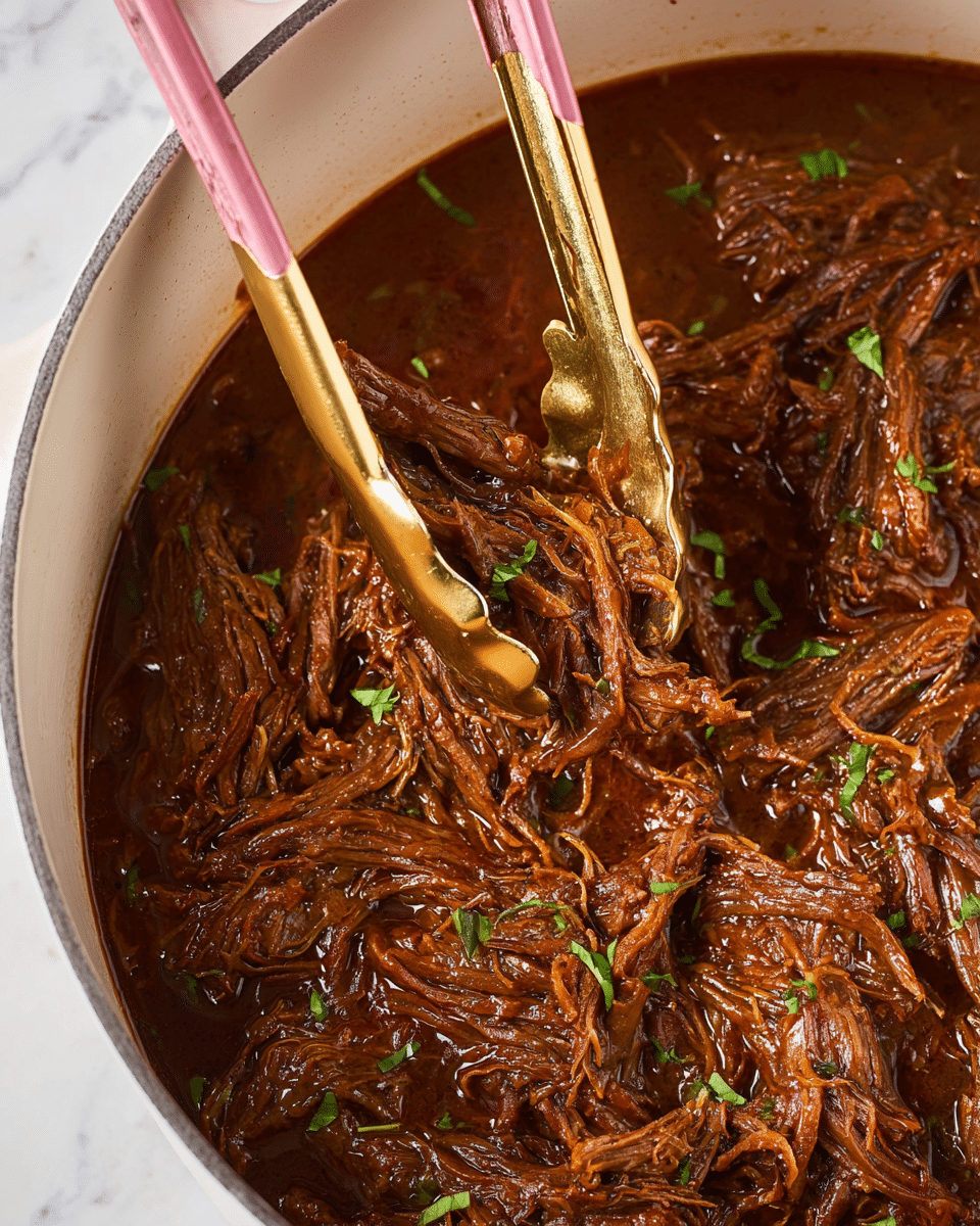 The image shows a close-up of shredded, cooked beef in a rich, dark brown sauce, with visible small pieces of green herbs scattered on top. The beef strands are tender and glossy, sitting in a pool of thick, oily sauce inside a white pot. A pair of kitchen tongs with pink silicone tips and golden handles is gripping some of the beef, lifting it slightly above the sauce. The background surface is a white marbled texture. photo taken with an iphone --ar 4:5 --v 7