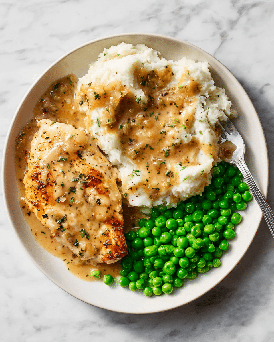 A white plate on a white marbled texture holds a meal with three main parts: on the left, a golden-brown grilled chicken breast covered lightly with a creamy brown gravy that has small bits of herbs and onions; above, fluffy white mashed potatoes topped with the same creamy brown gravy scattered unevenly across the surface; and on the right, a neat pile of bright green peas with a smooth, round texture. A silver fork rests on the right edge of the plate, slightly touching the peas. The image is sharp with natural lighting highlighting the textures and colors of the food. photo taken with an iphone --ar 4:5 --v 7